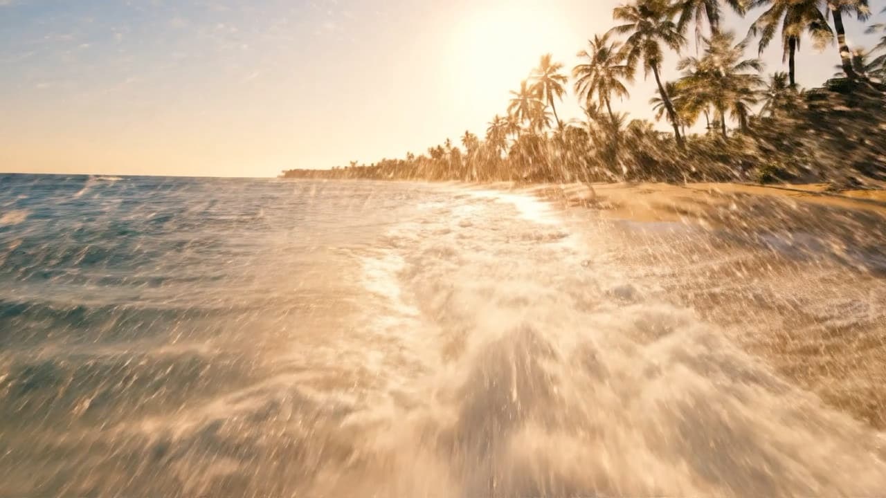 Cinematic drone shot flying low over turquoise ocean waves crashing on a tropical beach at golden hour, camera gliding smoothly, water spray catching sunlight